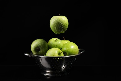 Photo of Green apple with water drops falling down into colander on black background