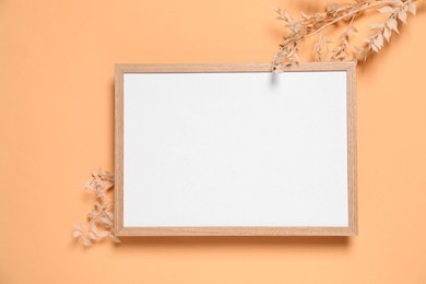 Photo of Empty photo frame and dry decorative plants on pale orange background, flat lay. Space for design