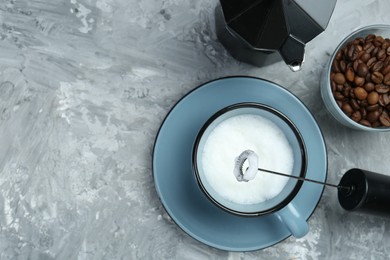 Photo of Mini mixer (milk frother), whipped milk in cup, coffee beans and moka pot on grey textured table, flat lay. Space for text