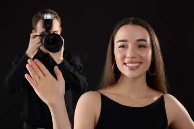 Photo of Professional photographer taking picture of beautiful young woman on black background, selective focus