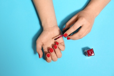Photo of Woman applying nail polish on color background, top view