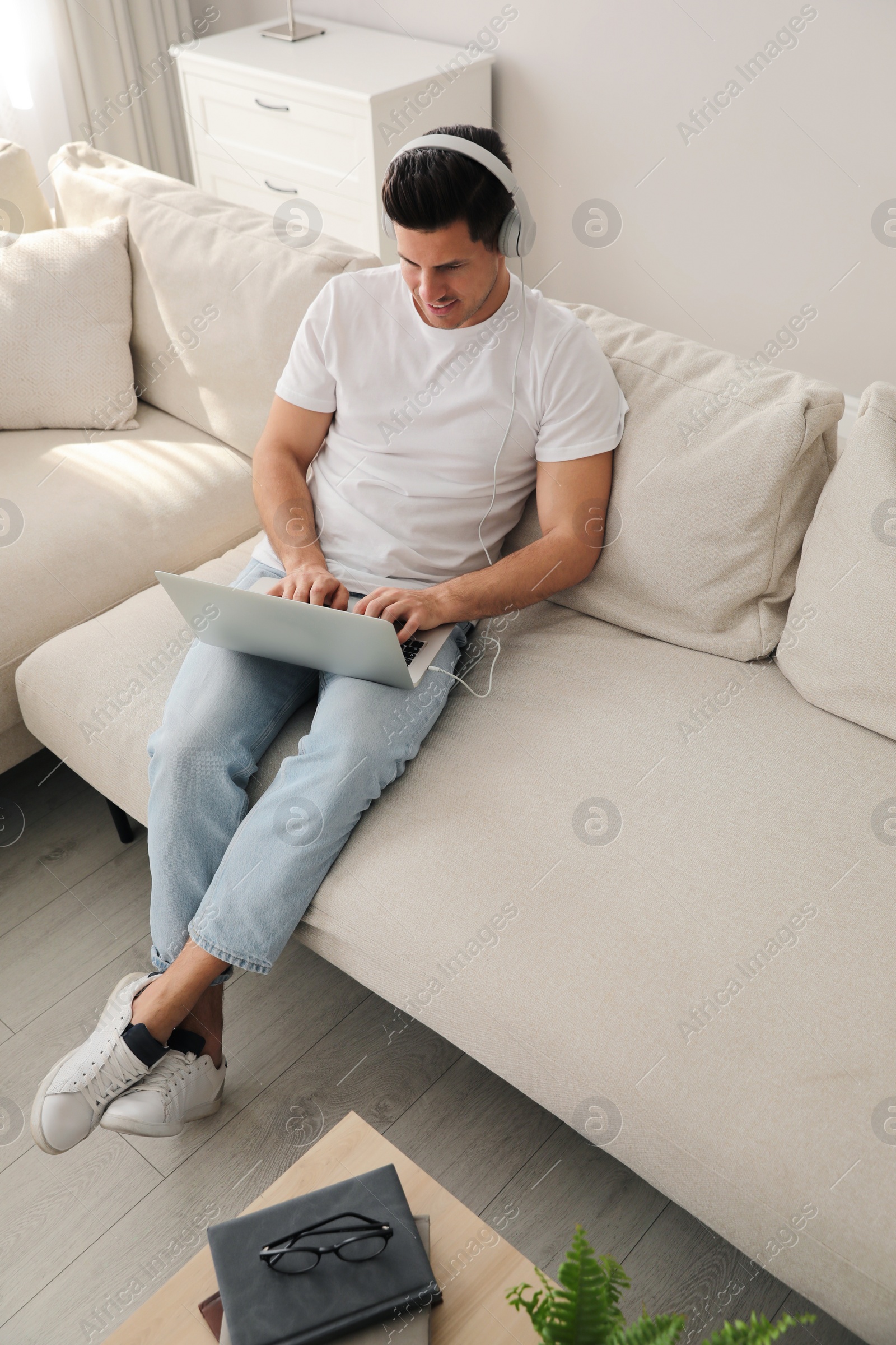 Photo of Man with laptop and headphones sitting on sofa at home