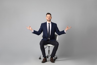 Photo of Handsome businessman meditating in office chair on grey background