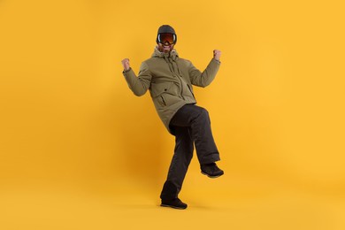 Photo of Winter sports. Cheerful man in ski suit and goggles on orange background