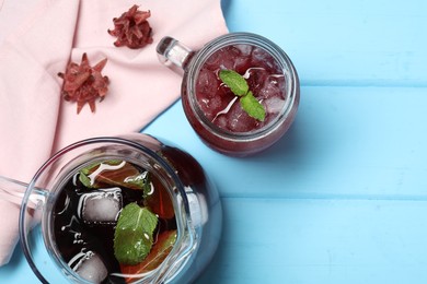 Photo of Delicious iced hibiscus tea with mint and dry flowers on light blue wooden table, flat lay. Space for text