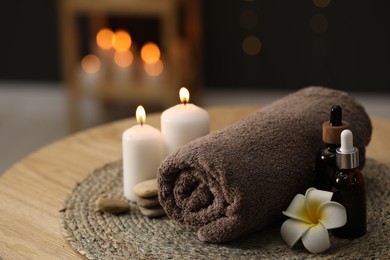 Photo of Spa composition. Rolled towel, cosmetic products, stones, burning candles and plumeria flower on table indoors, closeup