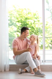 Photo of Young man with cute little girl near window at home