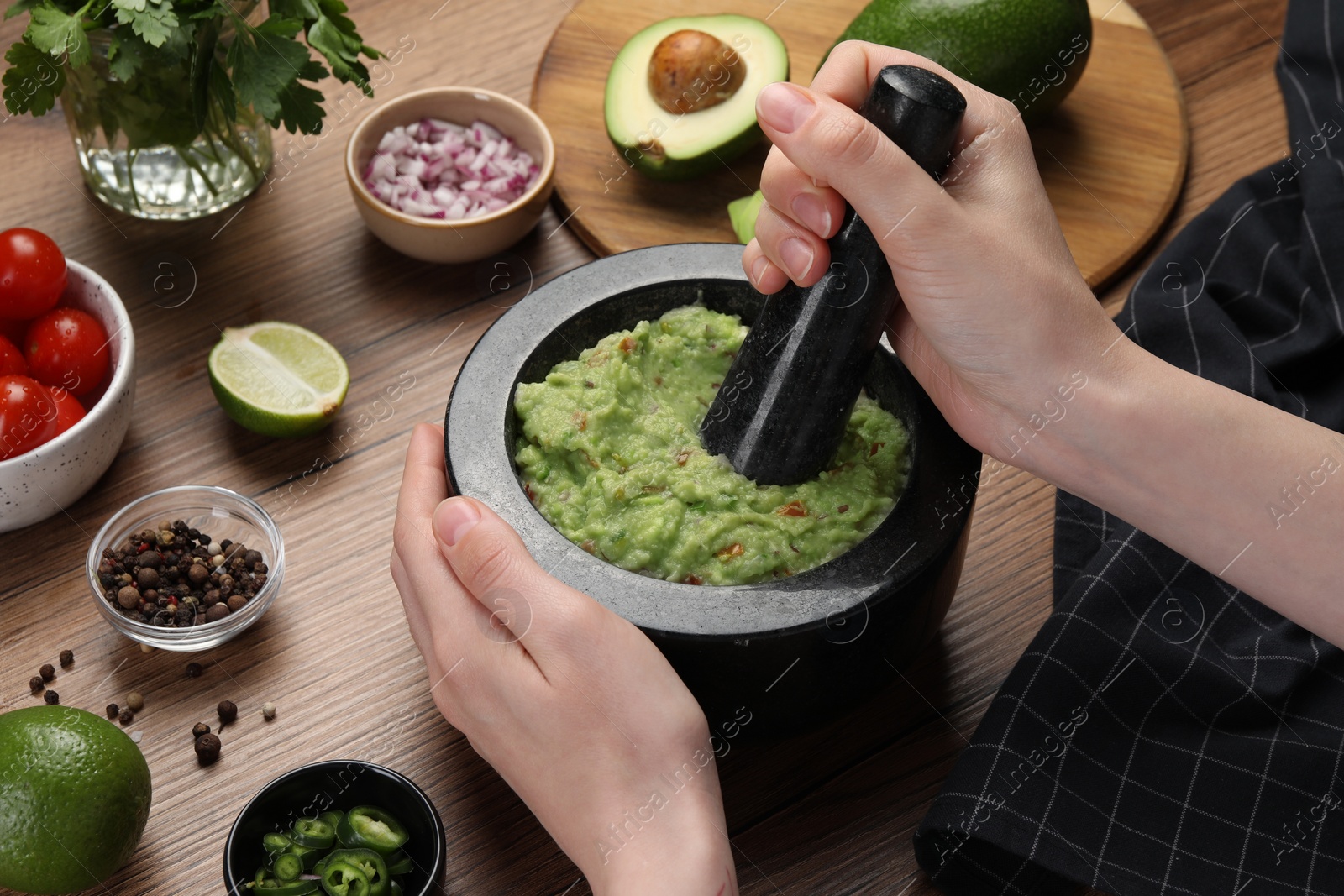 Photo of Woman preparing delicious guacamole at wooden table, closeup