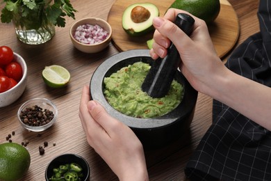 Photo of Woman preparing delicious guacamole at wooden table, closeup