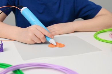 Photo of Boy drawing with stylish 3D pen at white table, closeup