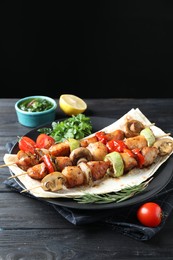 Photo of Delicious shish kebabs with vegetables served on black wooden table against dark background, space for text
