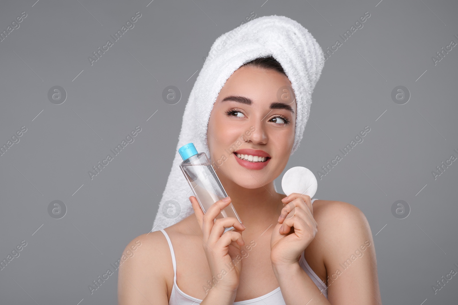 Photo of Beautiful woman in terry towel with makeup remover and cotton pad on gray background