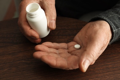 Photo of Senior man holding bottle and pill at table, closeup of hands