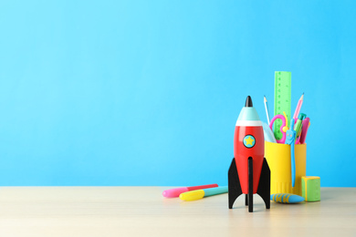 Photo of School stationery and rocket on wooden table against light blue background. Space for text