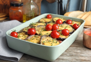 Photo of Baked eggplant with tomatoes and cheese in dishware on wooden table