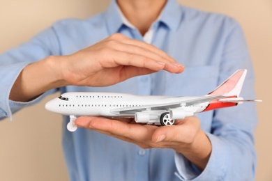 Photo of Insurance agent covering toy plane on color background, closeup. Travel safety concept