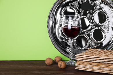 Photo of Symbolic Pesach (Passover Seder) items on wooden table against green background, space for text
