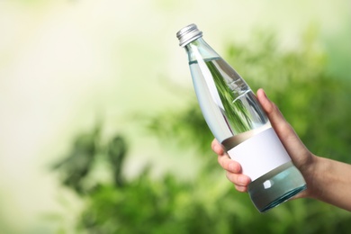 Photo of Woman holding bottle of water on blurred background. Space for text