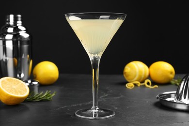 Photo of Martini glass of refreshing cocktail, fresh fruits, rosemary, shaker and hand citrus squeezer on black table