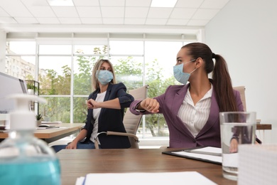 Photo of Office employees in masks greeting each other by bumping elbows at workplace