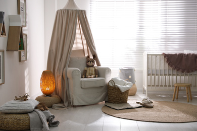 Photo of Stylish baby room interior with crib and comfortable armchair