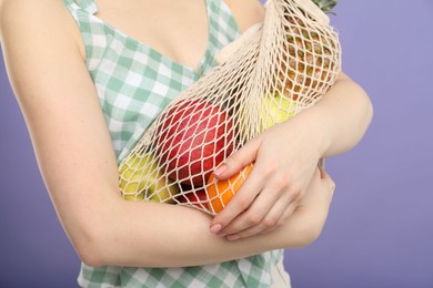 Photo of Woman with string bag of fresh fruits on violet background, closeup
