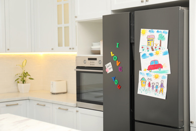 Photo of Modern refrigerator with child's drawings, note and magnets in kitchen. Space for text