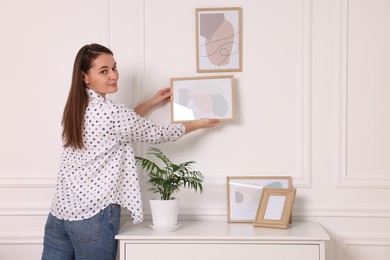 Photo of Woman hanging picture frame on white wall at home