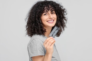 Photo of Young woman holding teeth whitening strips on light grey background
