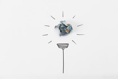 Photo of Composition with crumpled banknote and drawing of lamp bulb on white background, top view. Creative concept