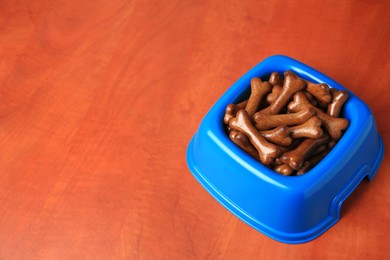 Photo of Blue bowl with bone shaped dog cookies on wooden table, space for text