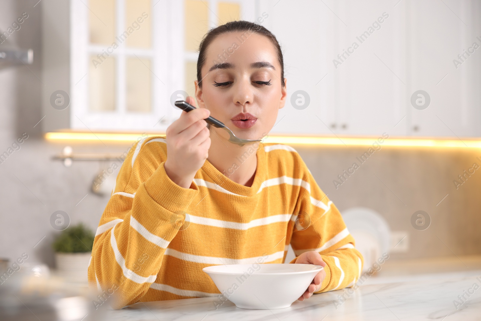 Photo of Beautiful woman eating tasty soup at white table in kitchen