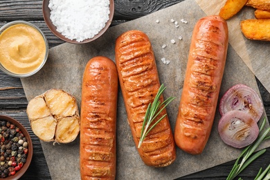 Photo of Flat lay composition with delicious grilled sausages on wooden table. Barbecue food