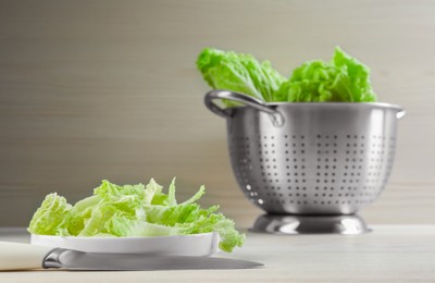 Photo of Cut fresh ripe Chinese cabbage and knife on white table against light wooden background. Space for text