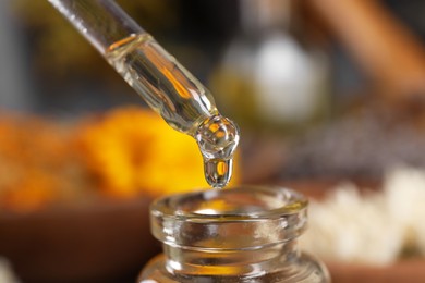 Photo of Dripping herbal essential oil from pipette into bottle on blurred background, closeup