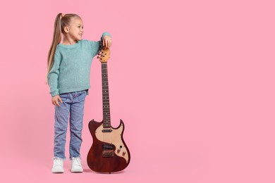 Photo of Happy girl with electric guitar on pink background. Space for text
