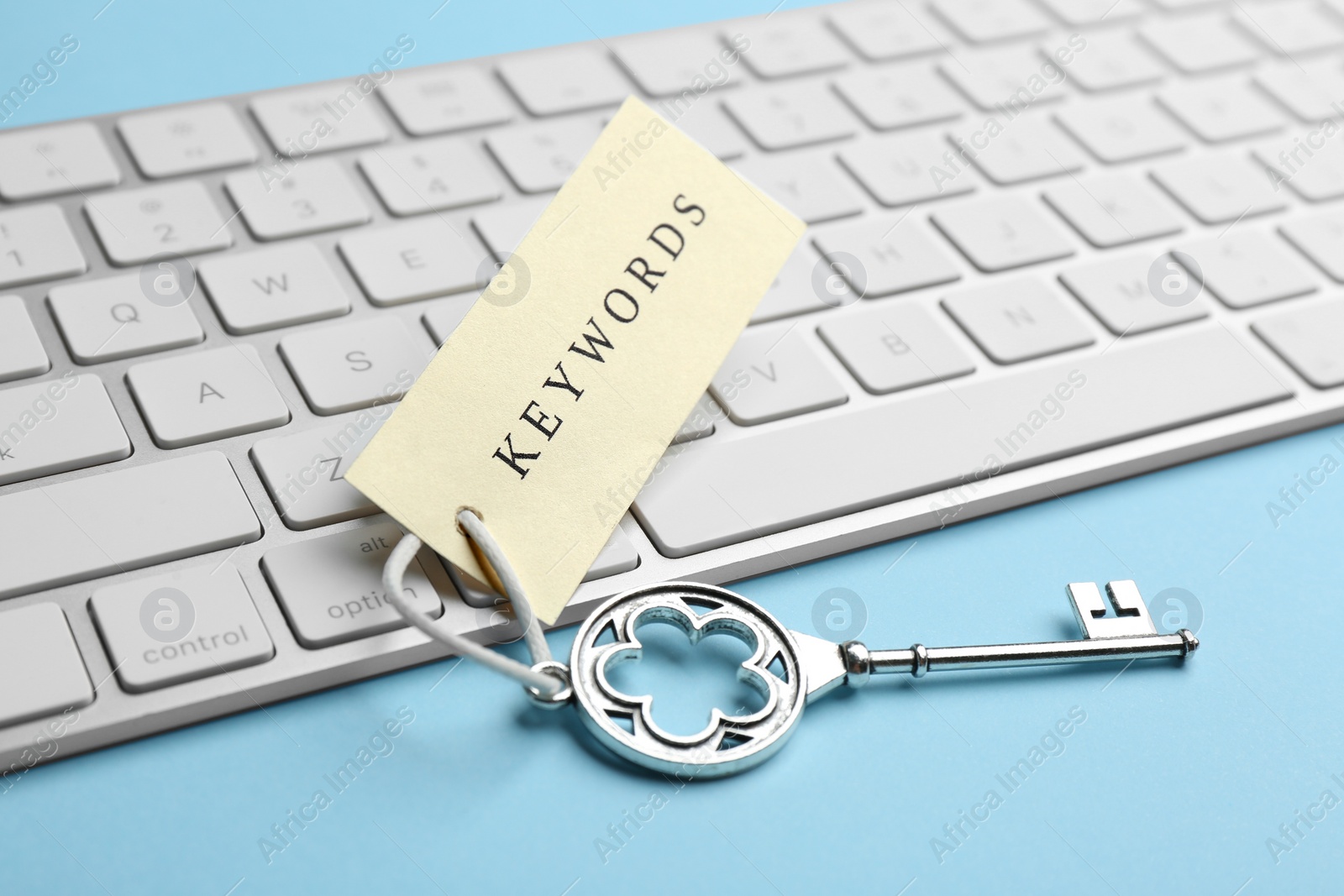 Photo of Keyboard, vintage key and tag with word KEYWORDS on light blue background, closeup