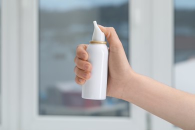 Photo of Woman holding nasal spray bottle indoors, closeup