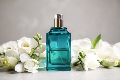 Photo of Bottle of perfume and beautiful flowers on light table