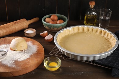 Photo of Pie tin with fresh dough, rolling pin and ingredients on wooden table. Making quiche