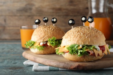 Photo of Cute monster burgers served on blue wooden table. Halloween party food