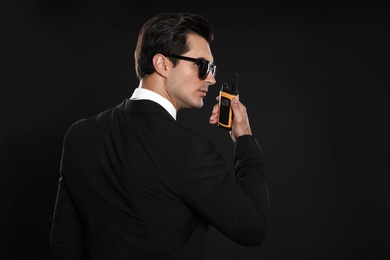 Photo of Male security guard in uniform using portable radio transmitter on dark background