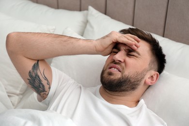 Photo of Young man suffering from migraine in bed