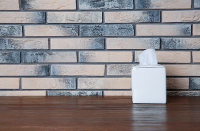 Photo of Napkin holder with paper serviettes on table against brick wall. Space for text