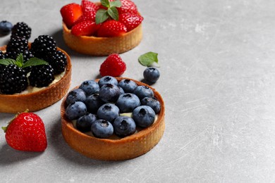 Photo of Tartlets with different fresh berries on light grey table, space for text. Delicious dessert
