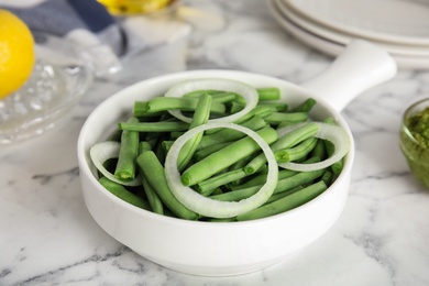Photo of Raw green beans and onion on white marble table, closeup