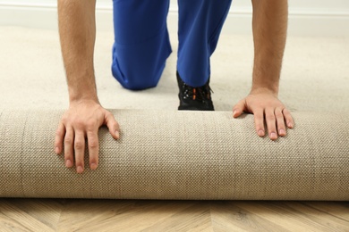 Photo of Worker rolling out new carpet flooring indoors, closeup
