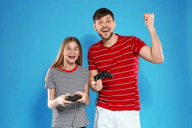 Photo of Emotional man and teenage girl playing video games with controllers on color background