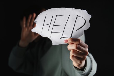 Photo of Woman holding piece of paper with word Help on black background, closeup. Domestic violence concept