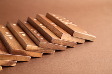 Photo of Fallen wooden domino tiles on brown background, closeup